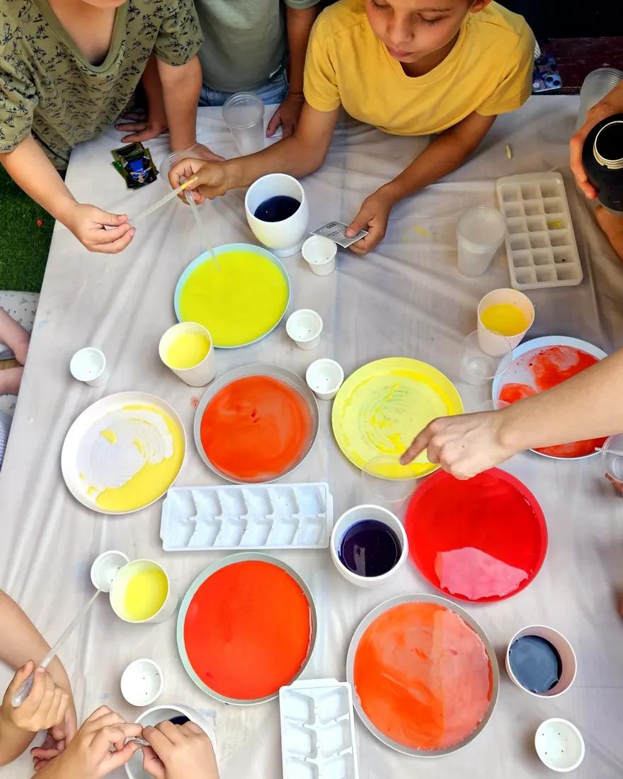 Niños mezclan témperas de colores en platos sobre la mesa, vista desde arriba.